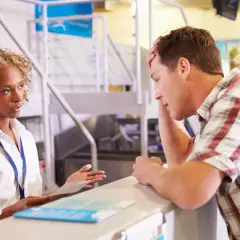 Zestresowany mężczyzna przy stanowisku check-in, rozmawia z pracownicą lotniska.