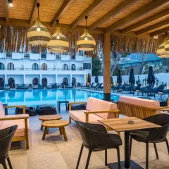 Relaks przy basenie w Heronissos Hotel Kreta. Jasne meble, wiklinowe lampy i tropikalna roślinność tworzą wakacyjny klimat.
