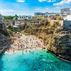 Malownicze bari plaże z białymi domami na klifach i turkusową wodą. Ludzie odpoczywają na kamienistej plaży i kąpią się w morzu.