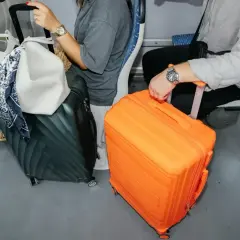 Podróżni z bagażem podręcznym: czarna walizka i jaskrawo pomarańczowa walizka stoją obok siebie w pociągu.