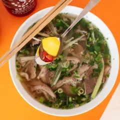 Aromatyczne wietnamskie jedzenie: miska pho z wołowiną, makaronem ryżowym, ziołami i plasterkami chili na łyżce.