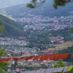 Widok na stolicę Bhutanu, Thimphu, z góry. W oddali widać gęsto zabudowane wzgórza, a na pierwszym planie wiszą kolorowe flagi modlitewne.