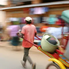 Madagaskar ludność w ruchu. Mężczyzna ciągnie wózek z koszem i towarami, pośród zamazanych postaci na targu.