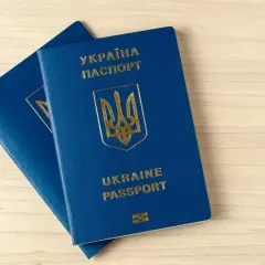 Dwa niebieskie paszporty biometryczne Ukrainy leżą na drewnianym blacie.