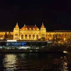 Nocny rejs po Dunaju w Budapeszcie. Oświetlony budynek i statek wycieczkowy odbijają się w wodzie.