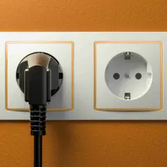 Dwa gniazdka elektryczne, jedno z wtyczką, na pomarańczowej ścianie. Typowe gniazdka w Turcji.