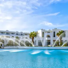 Basen z fontannami przed hotelem Club Palm Azur Djerba. Błękitna woda i biała architektura pod błękitnym niebem.