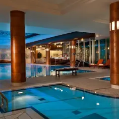 Basen w hotelu Radisson Blu Radebeul, z błękitną wodą, drewnianymi kolumnami i leżakami.