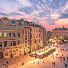 Zachód słońca nad Rynkiem Głównym w Krakowie, idealne miejsce na city break z Krakowa. Tłumy spacerują wśród kamienic i ogródków restauracyjnych.