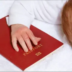 Dziecko z rudymi włosami śpi na białym ręczniku, jego dłoń spoczywa na czerwonym paszporcie. Czy do Hiszpanii potrzebny jest paszport?