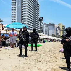 Meksyk zamieszki na plaży. Policjanci w pełnym rynsztunku patrolują brzeg, podczas gdy turyści odpoczywają pod parasolami.