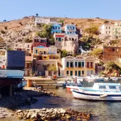 Kolorowe domy na zboczu góry, łodzie w zatoce i kamienista plaża na wyspie Symi.