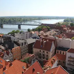 Widok na Toruń z lotu ptaka: Wisła, most kolejowy i zabytkowa zabudowa z czerwonymi dachami. Karta EKUZ Toruń.