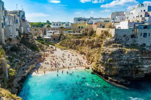 Malownicze bari plaże z białymi domami na klifach i turkusową wodą. Ludzie odpoczywają na kamienistej plaży i kąpią się w morzu.