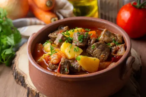 Gulasz wołowy, klasyk kuchni węgierskiej, w glinianej misie. Mięso, ziemniaki i warzywa w aromatycznym sosie.