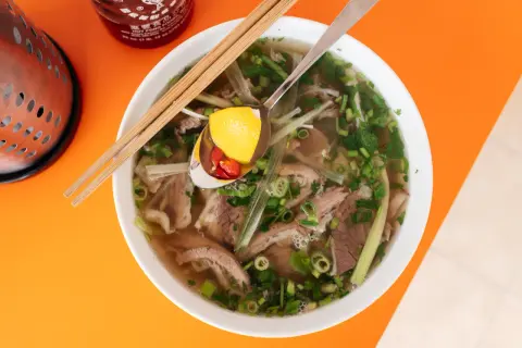 Aromatyczne wietnamskie jedzenie: miska pho z wołowiną, makaronem ryżowym, ziołami i plasterkami chili na łyżce.