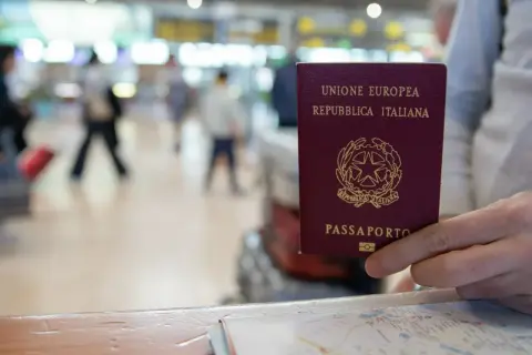 Włoski paszport w dłoni, na tle lotniska. Czy do Finlandii potrzebny jest paszport? Tak, jeśli nie jesteś obywatelem UE.