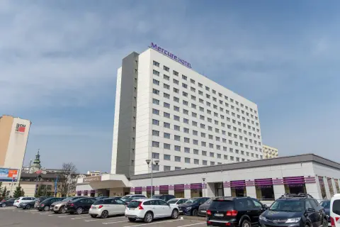 Hotel Mercure Gdynia z parkingiem pełnym samochodów. Elegancki budynek hotelu góruje nad parkingiem.