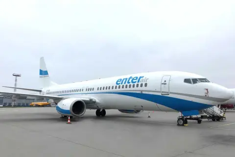 Biały samolot Enter Air z niebieskimi pasami na tle pochmurnego nieba. Gotowy do startu, by zabrać pasażerów w podróż.