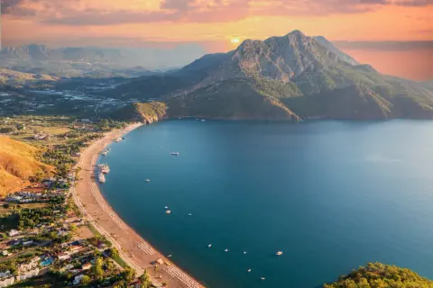 Widok z lotu ptaka na wybrzeże Turcji. Piękne turkusowe morze, piaszczysta plaża z leżakami i góry w tle o zachodzie słońca.