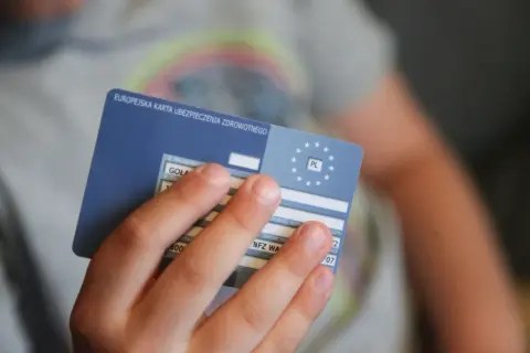 Dziecko trzyma kartę EKUZ, europejskie ubezpieczenie zdrowotne, gotowe na podróż.
