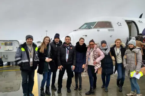 Grupa osób pozuje przed samolotem Bombardier Q400, z logo IATA na kadłubie.