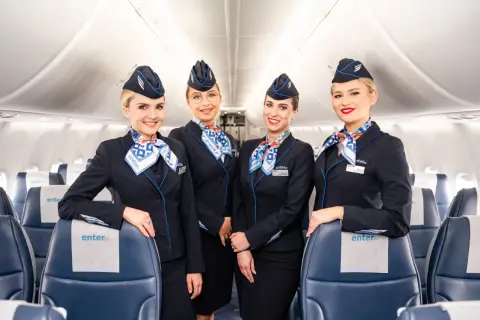 Uśmiechnięte stewardessy linii Enter Air w granatowych mundurkach i chustach z logo firmy, gotowe do lotu.
