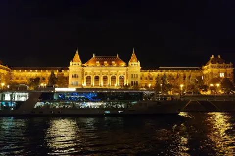Nocny rejs po Dunaju w Budapeszcie. Oświetlony budynek i statek wycieczkowy odbijają się w wodzie.