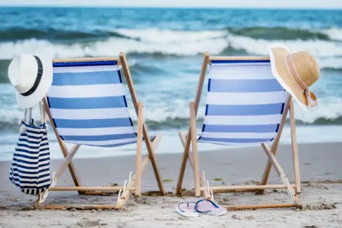 Dwa leżaki na plaży, gotowe na idealny weekend nad morzem. W tle widać morze i fale.
