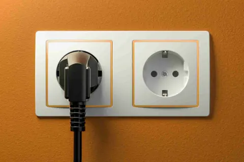 Dwa gniazdka elektryczne, jedno z wtyczką, na pomarańczowej ścianie. Typowe gniazdka w Turcji.