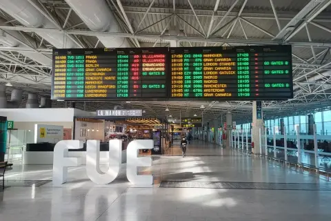 Tablica odlotów na lotnisku, z widocznym napisem "FUE". Informacje o lotach, w tym boarding, wskazują na podróż.