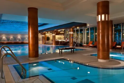 Basen w hotelu Radisson Blu Radebeul, z błękitną wodą, drewnianymi kolumnami i leżakami.