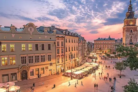 Zachód słońca nad Rynkiem Głównym w Krakowie, idealne miejsce na city break z Krakowa. Tłumy spacerują wśród kamienic i ogródków restauracyjnych.