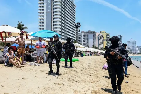 Meksyk zamieszki na plaży. Policjanci w pełnym rynsztunku patrolują brzeg, podczas gdy turyści odpoczywają pod parasolami.