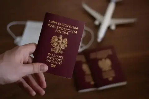 Dłoń trzyma polski paszport. Obok leżą kolejne dokumenty, maseczka i model samolotu. Planujesz podróż i zastanawiasz się, jak wyrobić paszport?