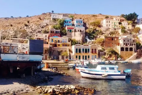 Kolorowe domy na zboczu góry, łodzie w zatoce i kamienista plaża na wyspie Symi.