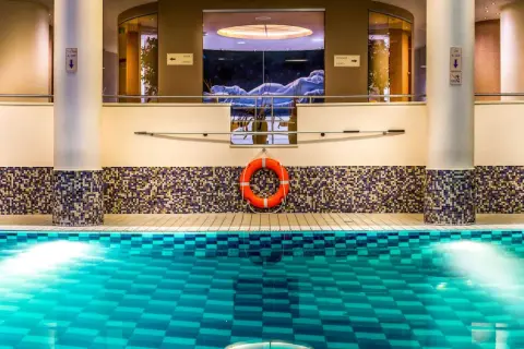 Basen w Radisson Blu Szczecin. Błękitna woda, mozaikowa ściana i rzeźba w tle.