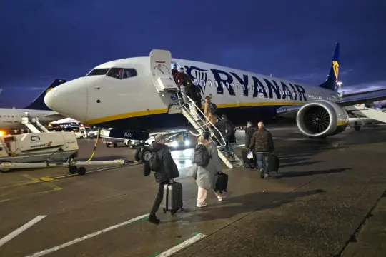 Pasażerowie z bagażami wchodzą po schodkach do samolotu Ryanair. Może to być opóźniony lot, bo jest już ciemno.