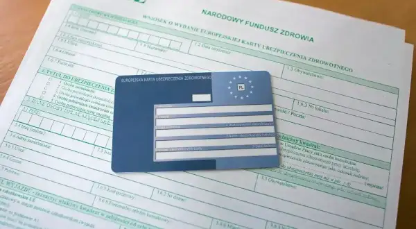 Wniosek o EKUZ. Ile się czeka na kartę? Dokumenty i karta ubezpieczenia zdrowotnego leżą na stole.