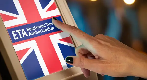 Dłoń dotyka ekranu z flagą Wielkiej Brytanii i napisem ETA Electronic Travel Authorization. To krok do uzyskania wizy do Anglii.