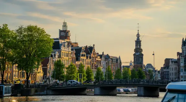 Złota godzina nad kanałem, gdzie jest Amsterdam. Wąskie kamienice, most pełen rowerów i łodzie na wodzie.