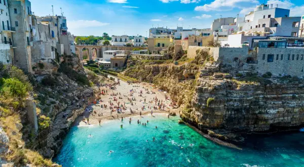Malownicze bari plaże z białymi domami na klifach i turkusową wodą. Ludzie odpoczywają na kamienistej plaży i kąpią się w morzu.