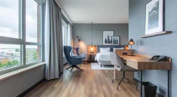 Nowoczesny pokój w **Radisson Blu Hotel Rostock** z widokiem na miasto, łóżkiem, fotelem i biurkiem.