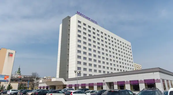 Hotel Mercure Gdynia z parkingiem pełnym samochodów. Elegancki budynek hotelu góruje nad parkingiem.
