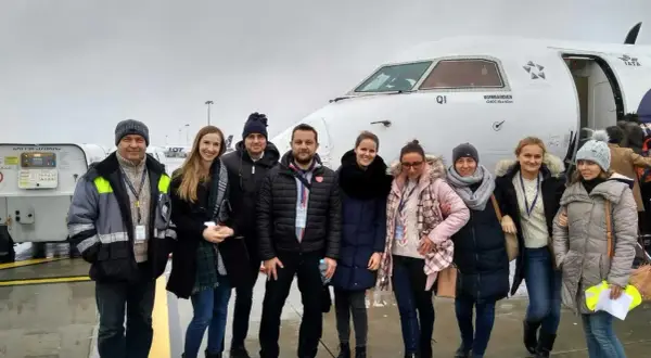 Grupa osób pozuje przed samolotem Bombardier Q400, z logo IATA na kadłubie.