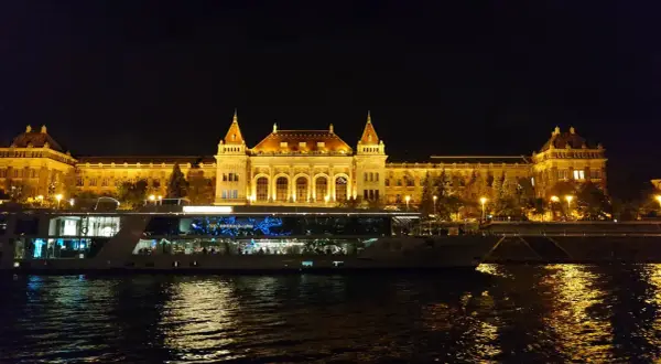Nocny rejs po Dunaju w Budapeszcie. Oświetlony budynek i statek wycieczkowy odbijają się w wodzie.