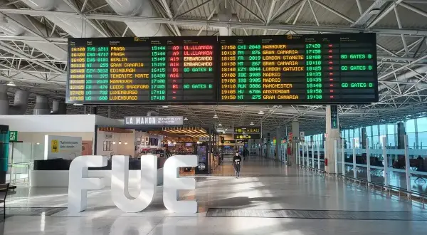 Tablica odlotów na lotnisku, z widocznym napisem "FUE". Informacje o lotach, w tym boarding, wskazują na podróż.