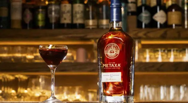 Butelka greckiego alkoholu Metaxa 12 gwiazdek i kieliszek z ciemnym trunkiem na tle baru.