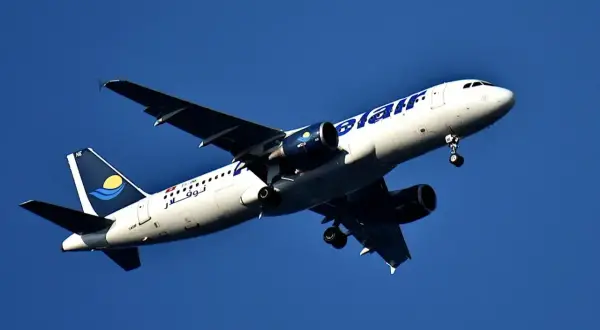 Samolot linii nouvelair z wysuniętym podwoziem wznosi się na tle błękitnego nieba.