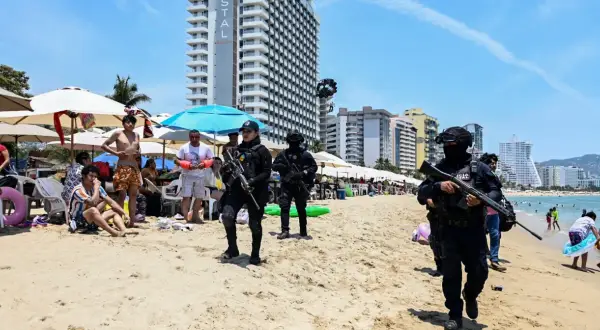 Meksyk zamieszki na plaży. Policjanci w pełnym rynsztunku patrolują brzeg, podczas gdy turyści odpoczywają pod parasolami.